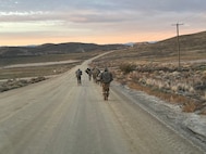 Soldiers ruck march down a dirt road.