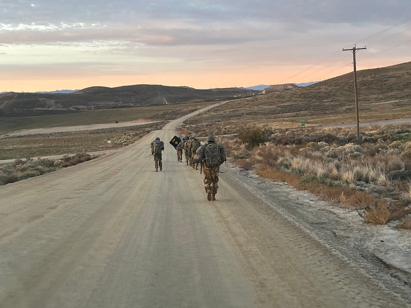 Soldiers ruck march down a dirt road.
