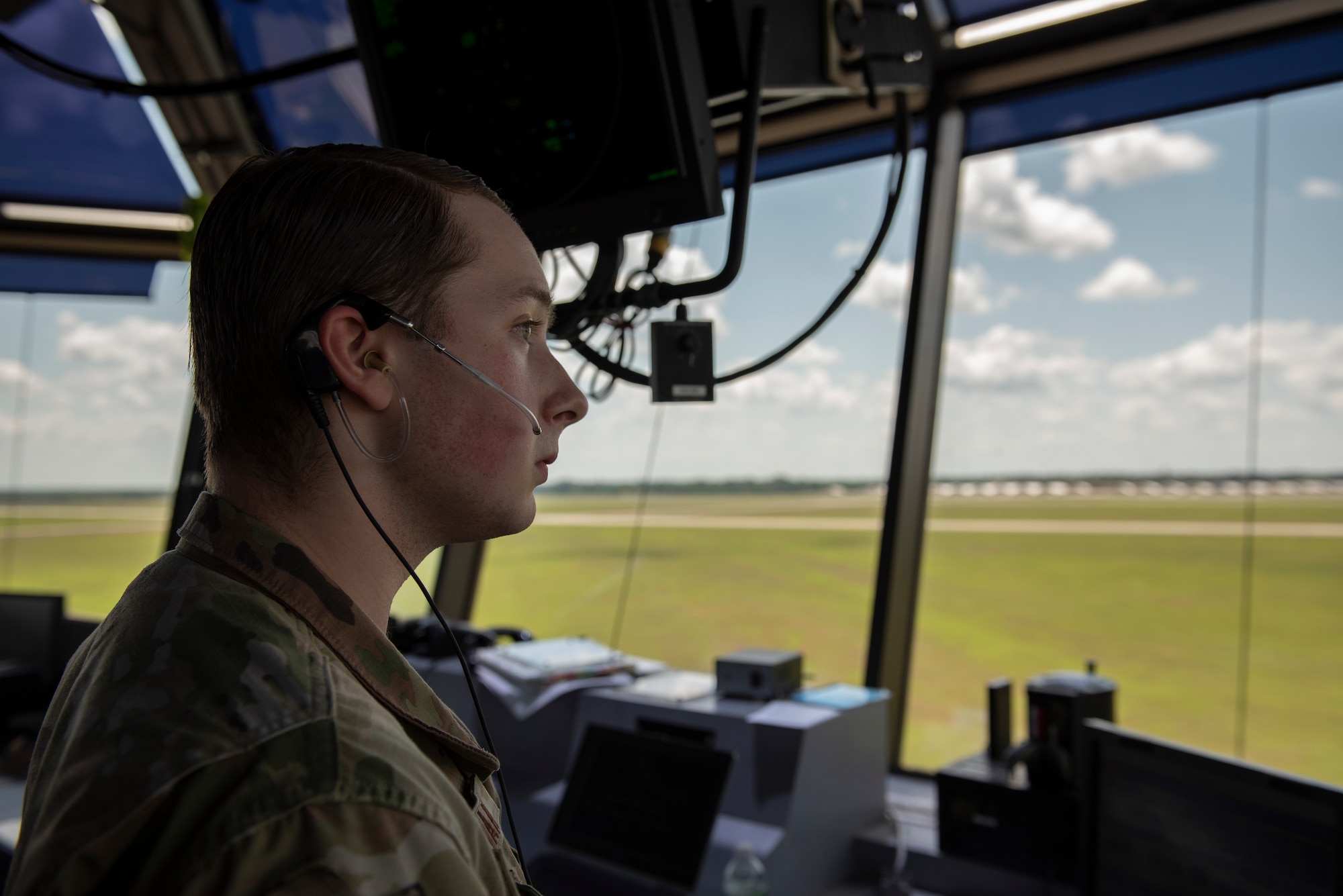 A photo of an airman with an ear piece in his ear looking out over the flight line.