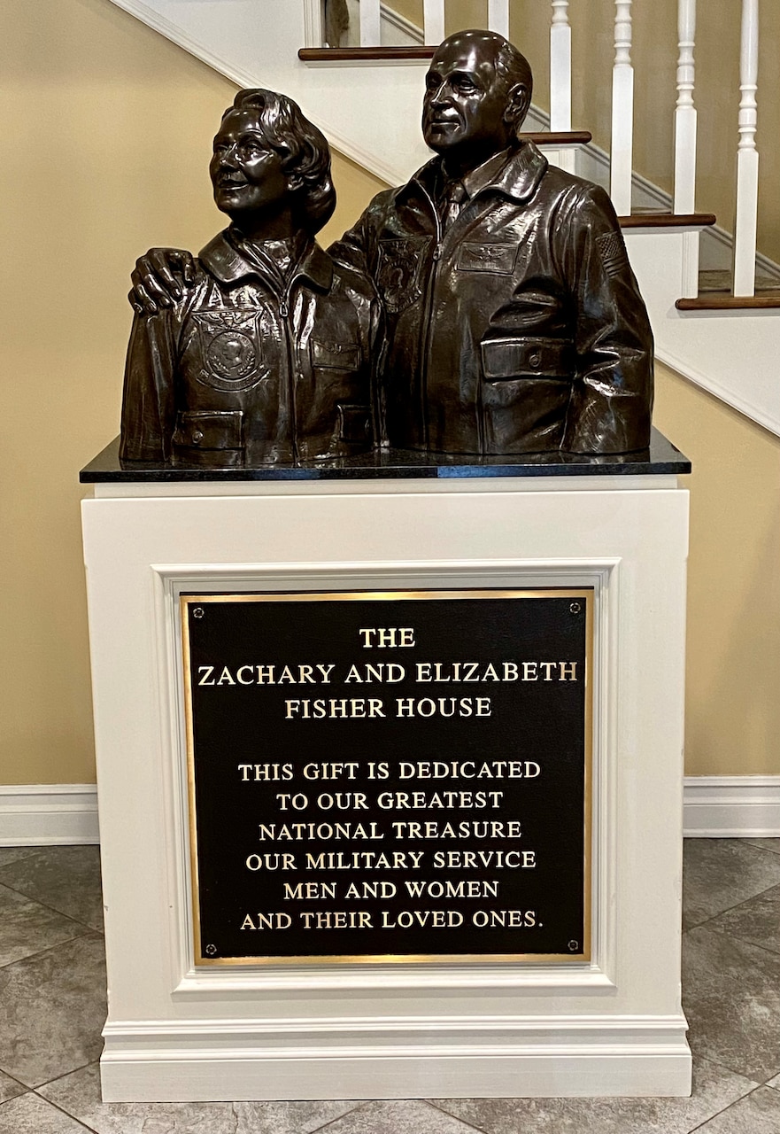 A bust of a man and woman sits atop a stand that bears a plaque that bears the words “The Zachary and Elizabeth Fisher House.”