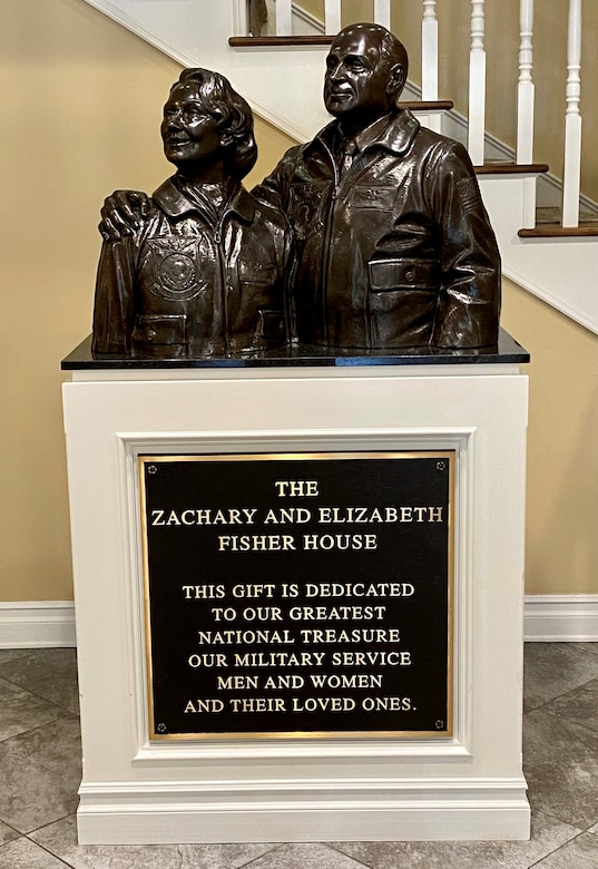 A bust of a man and woman sits atop a stand that bears a plaque that bears the words “The Zachary and Elizabeth Fisher House.”