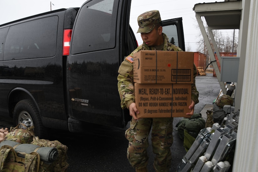 Spc. Steven Romero of the Alaska Army National Guard, 297th Military Police Company, loads MREs into a military vehicle in preparation to travel to Manley Hot Springs, Alaska, May 12, 2022, to support flood recovery operations. The Guardsmen will carry enough food and water to sustain themselves while they assist with cleanup and flood recovery efforts. (Alaska National Guard photo by Senior Master Sgt. Julie Avey)