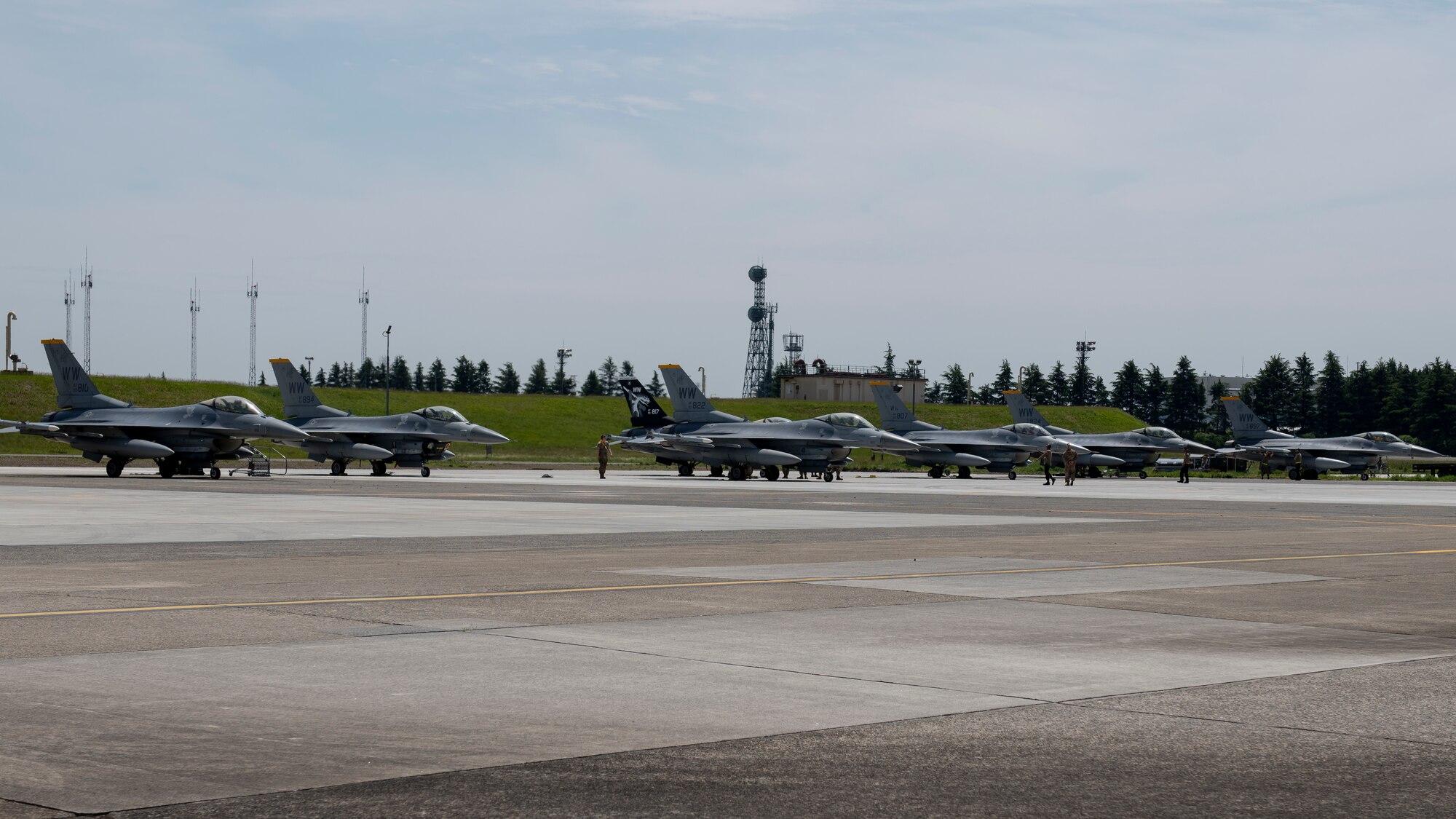 Seven F-16C Fighting Falcon fighter jets sit on a airport parking spot.