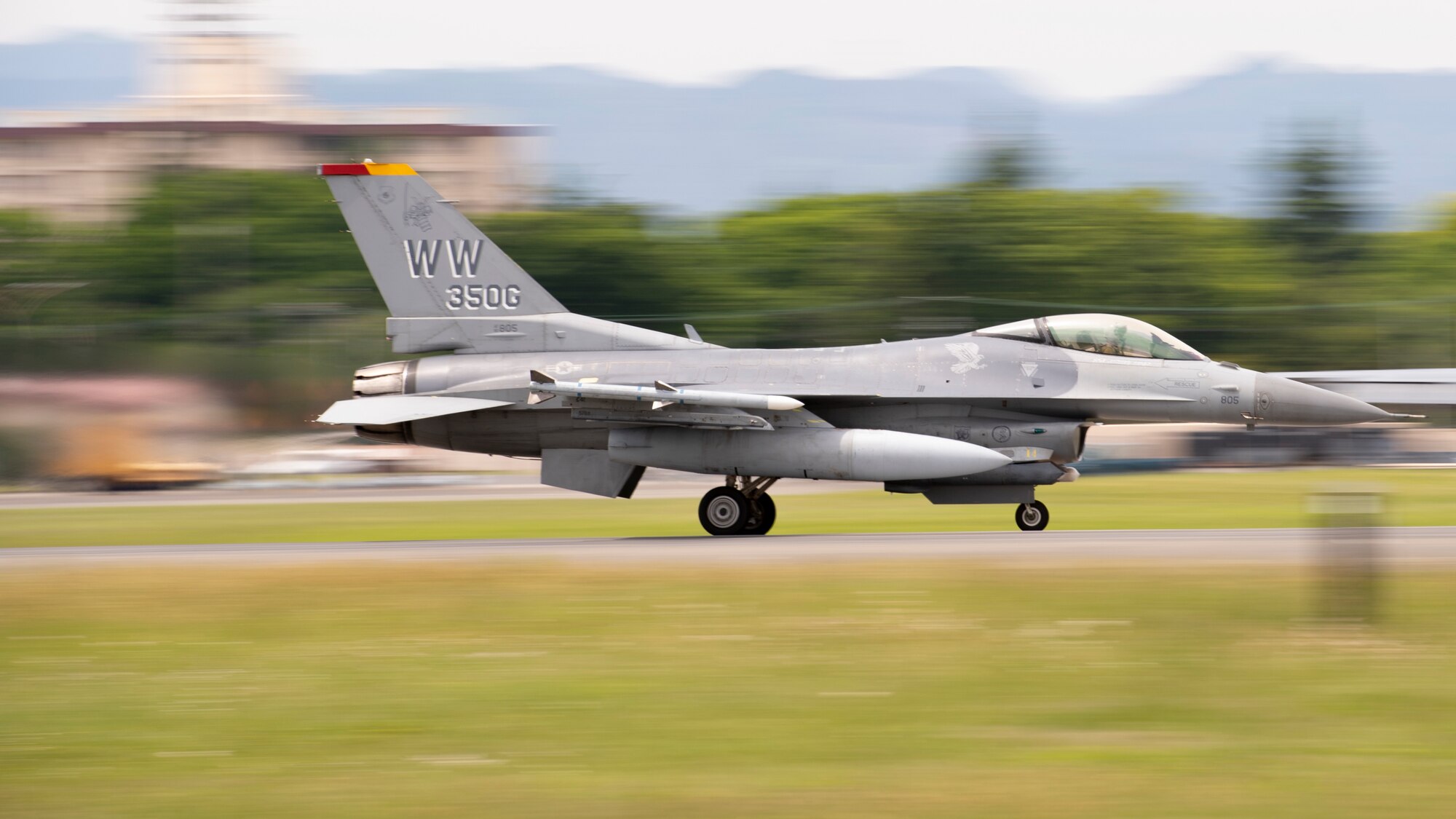 A sideways closeup view of a fighter jet speeding down the runway for takeoff.