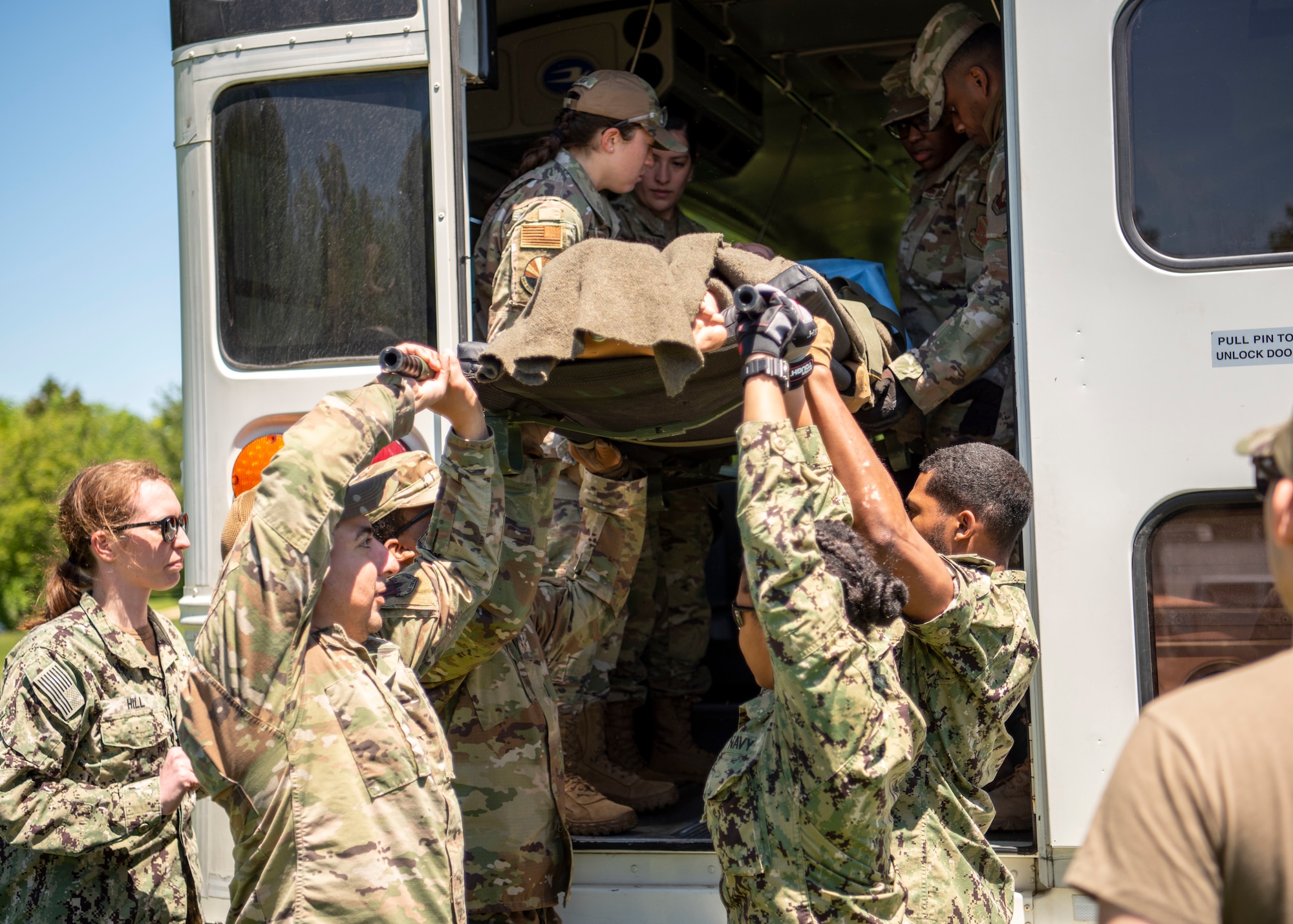 Airmen and Sailors work together to lower a gurney out of an ambulance bus during the Expeditionary Medical Support System exercise at Joint Base Andrews, Md., May 10, 2022.
