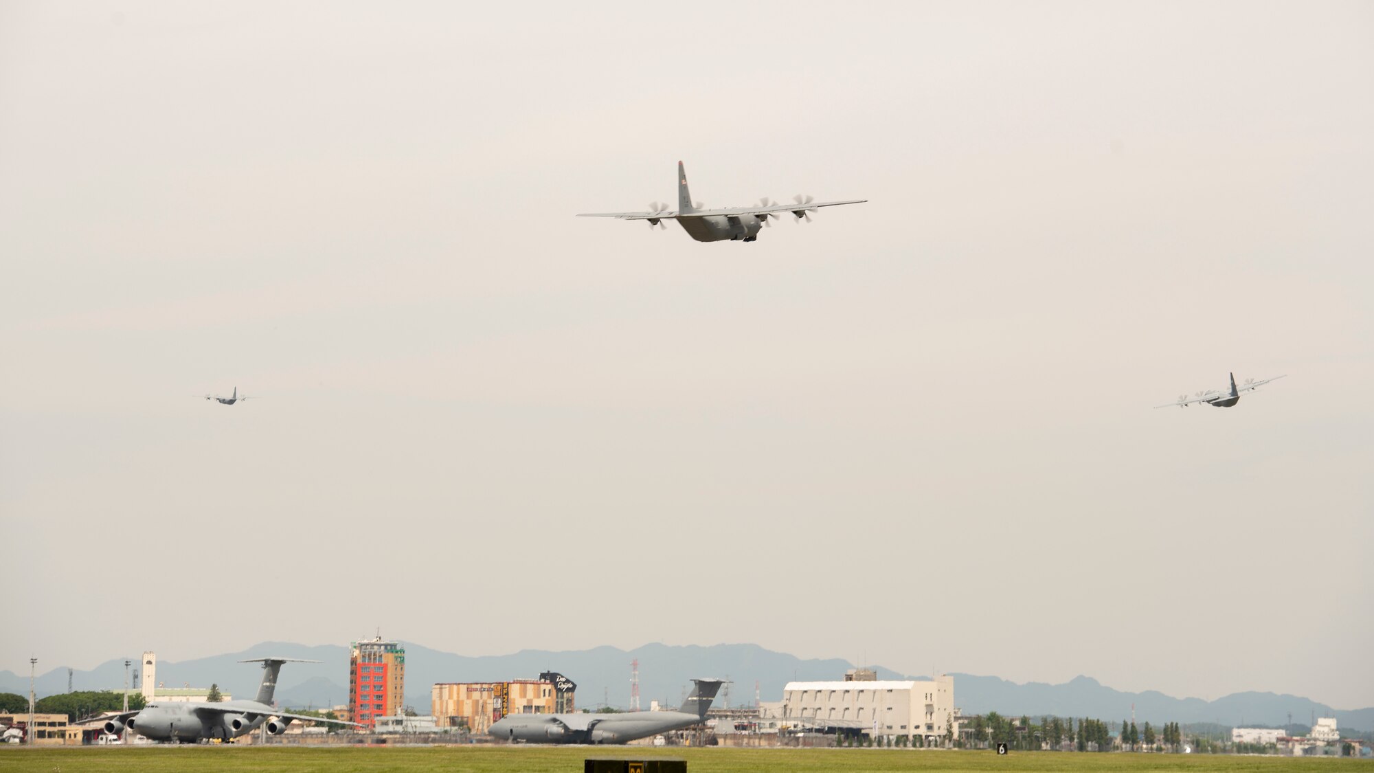 Three C-130J cargo aircraft fly in loose formation over the city of Fussa, Japan.