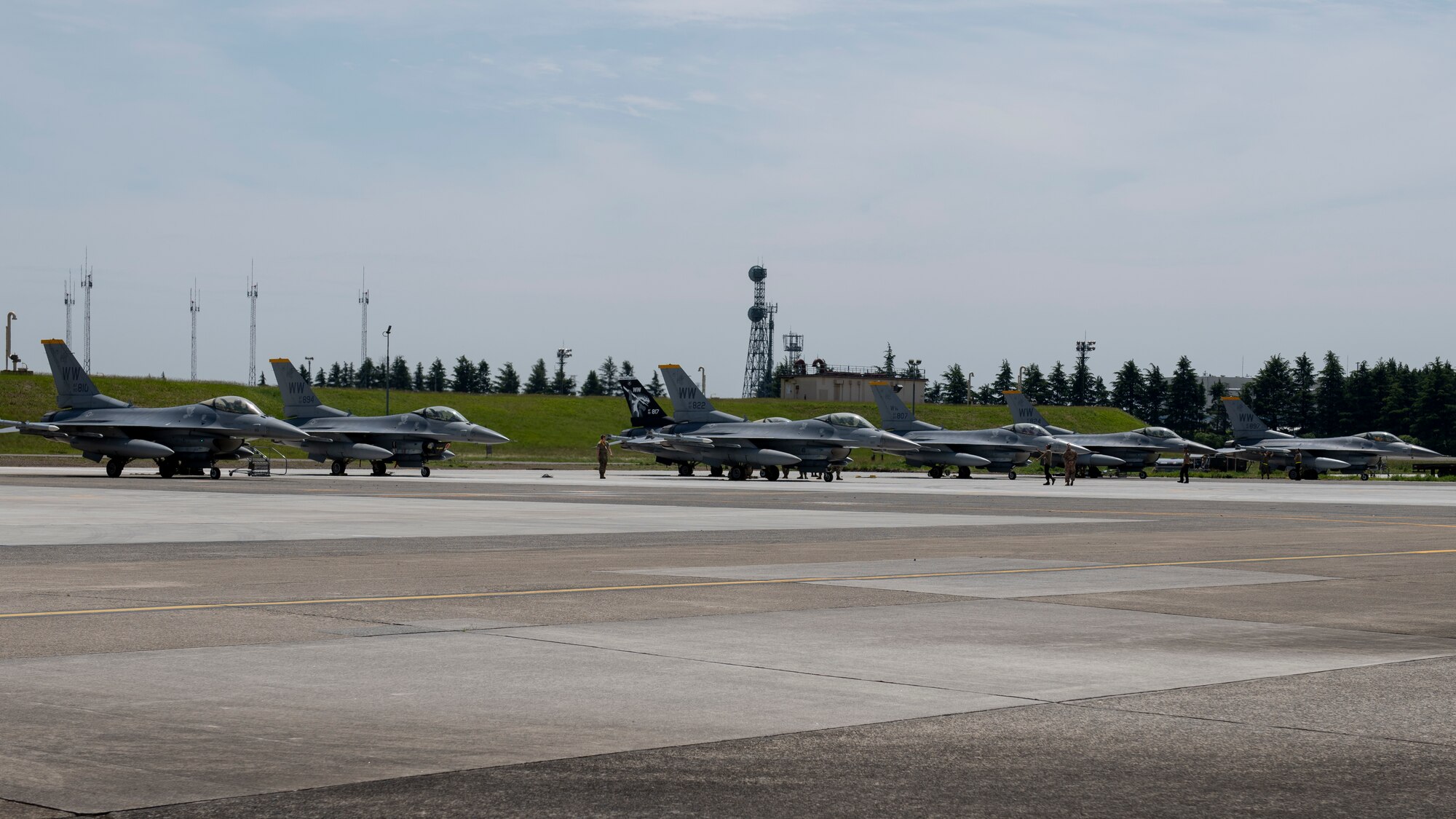 Seven F-16C Fighting Falcon fighter jets sit on a airport parking spot.