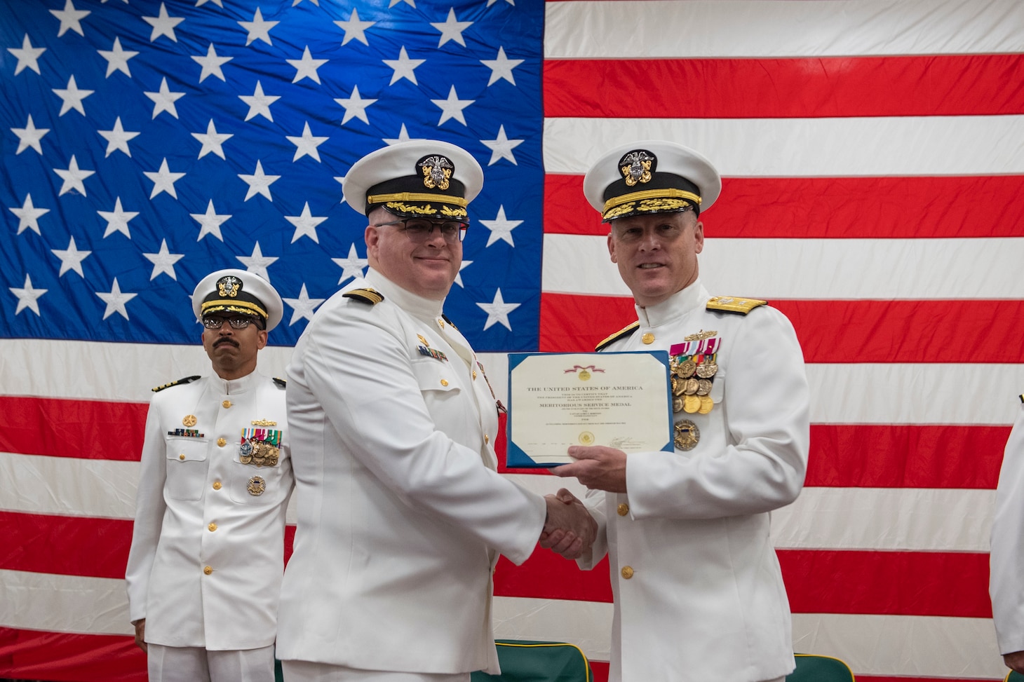 Capt. James T. Robinson, commanding officer of the forward-deployed amphibious transport dock ship USS Green Bay (LPD 20), receives the Meritorious Service Medal during a change-of-command ceremony in the ship’s vehicle stowage area. Green Bay, part of Amphibious Squadron 11, is operating in the U.S. 7th Fleet area of responsibility to enhance interoperability with allies and partners, and serve as a ready response force to defend peace and stability in the Indo-Pacific region. (U.S. Navy photo by Mass Communication Specialist Seaman Matthew Bakerian)