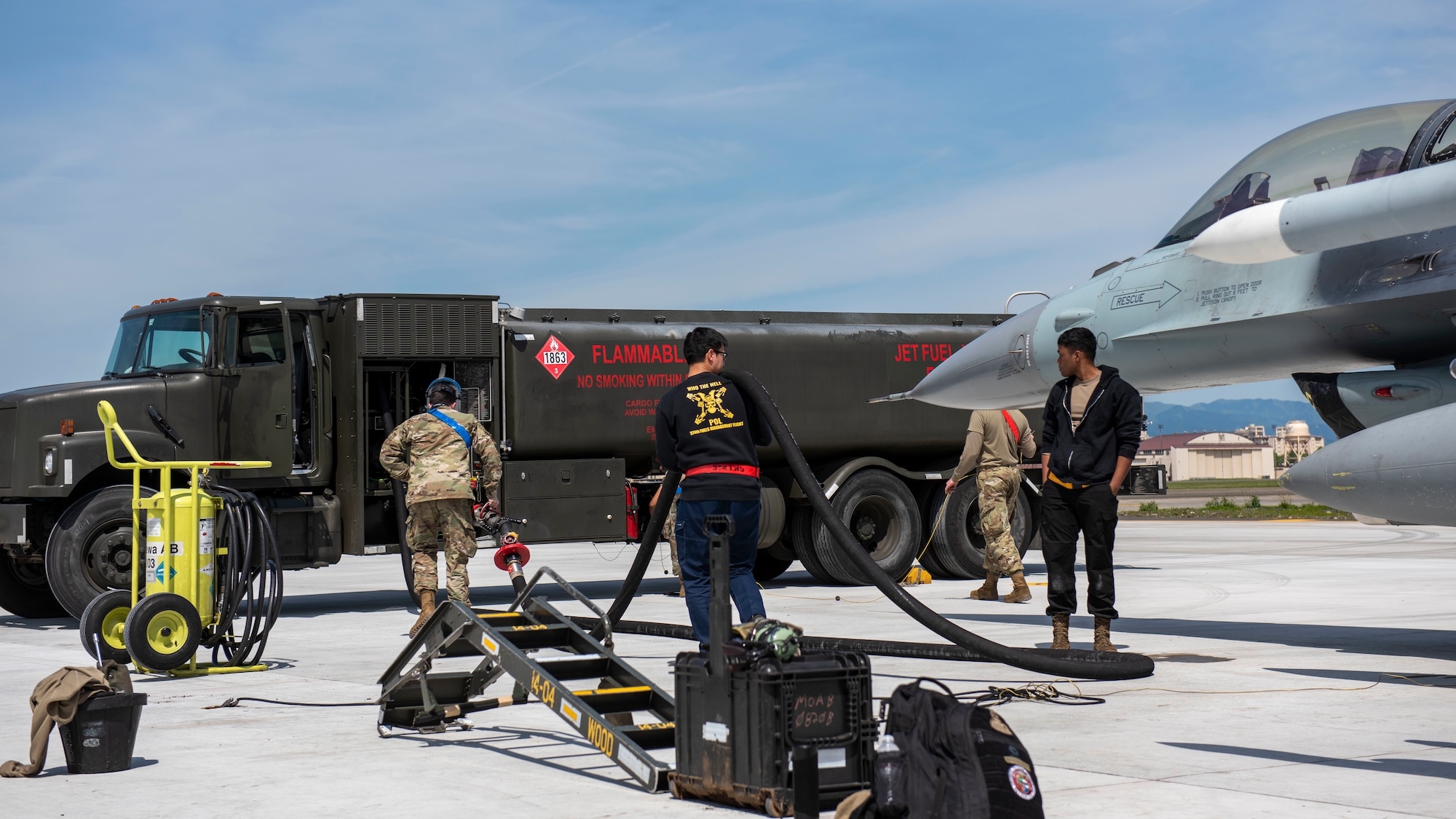 Airmen pull a fuel hose towards a refueling truck