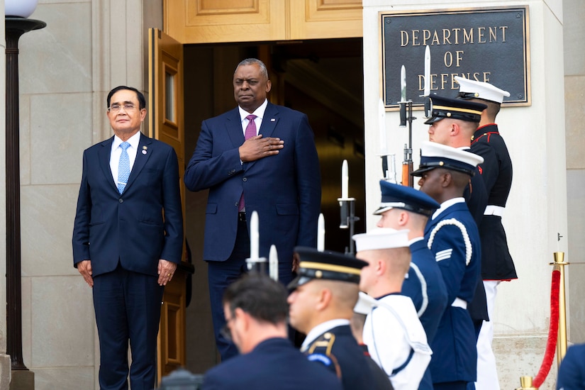 Two men stand side by side; one holds his hand over his chest.