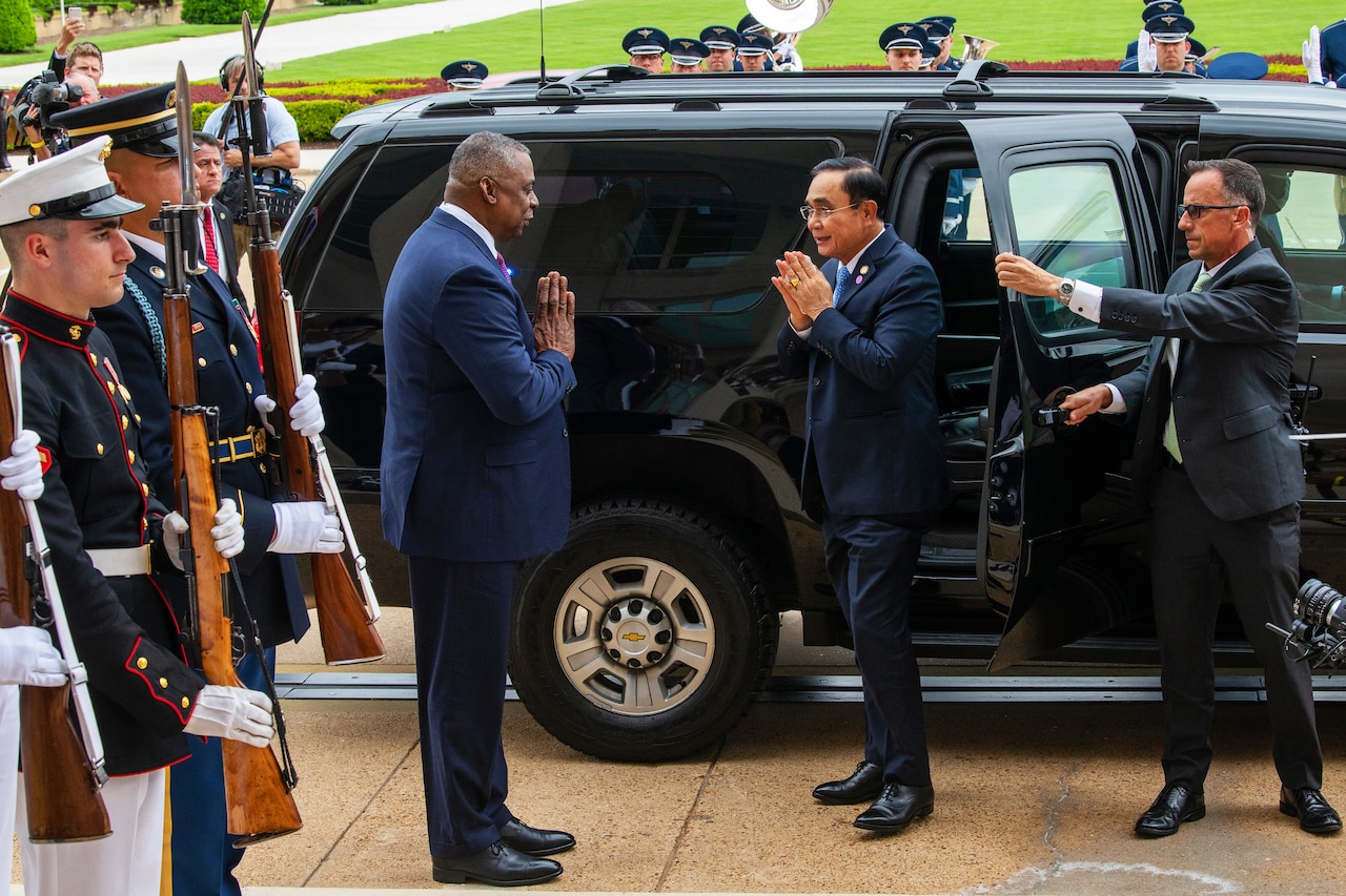 Two men greet each other standing next to a car.