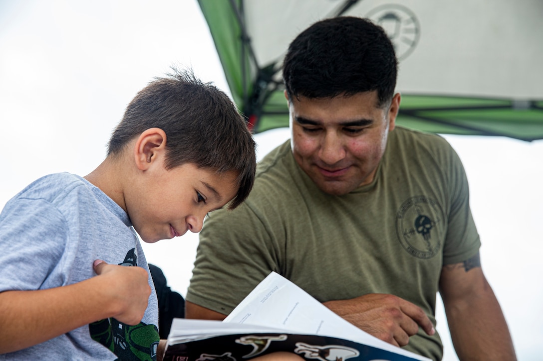 A Marine watches a young boy as he reads.
