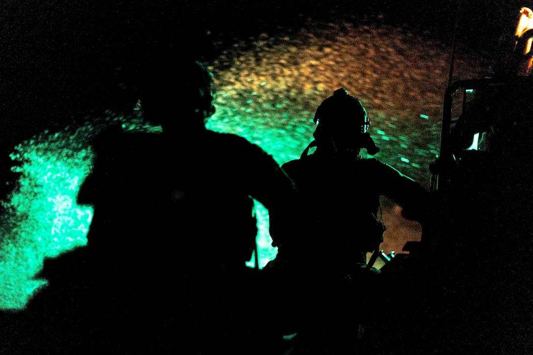 Two sailors shown in silhouette with a green light in the background.