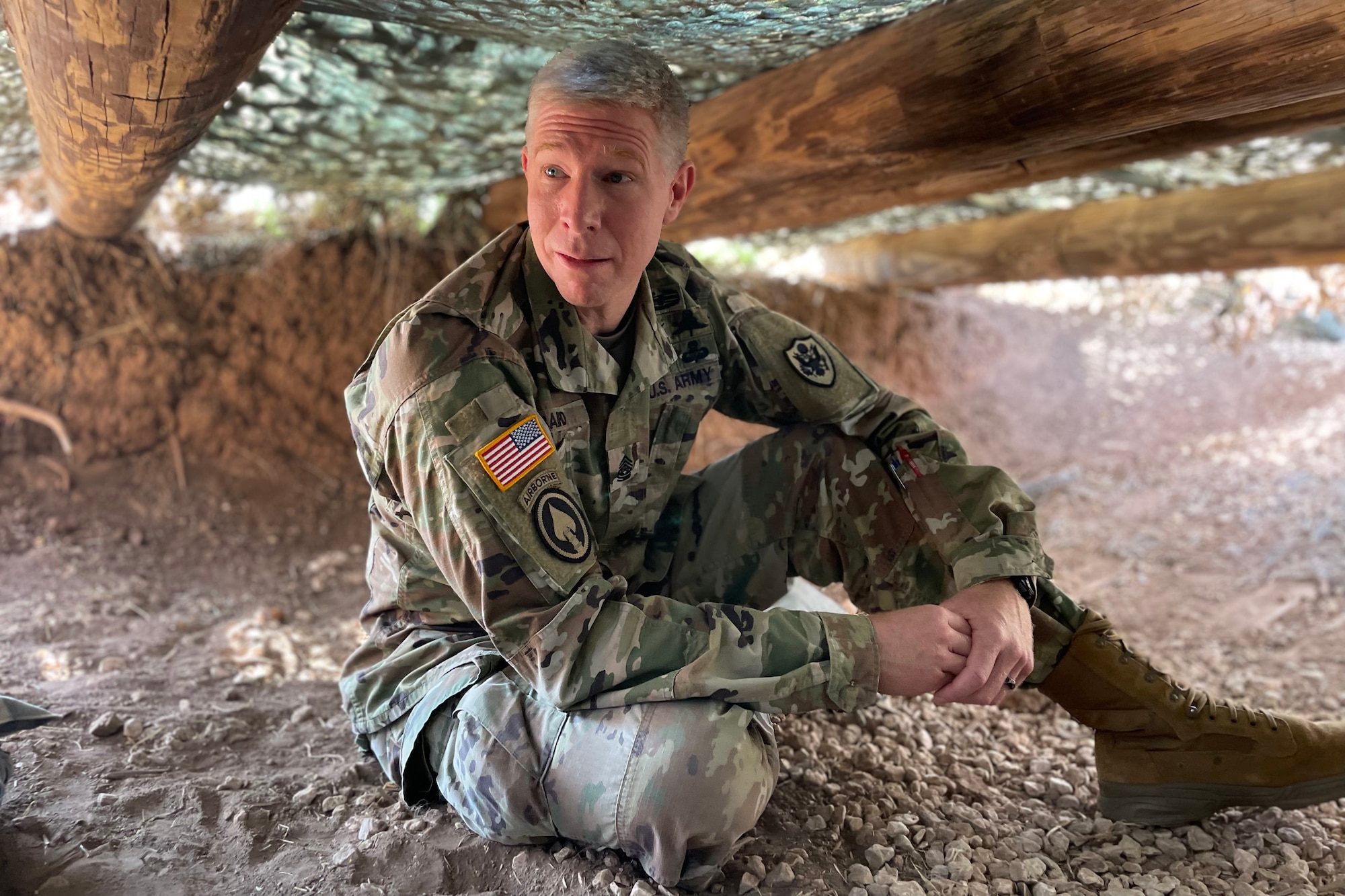 U.S. Army Command Sgt. Maj. Thomas Baird, National Geospatial-intelligence Agency command senior enlisted leader, crawled into a training foxhole to meet 344th Military Intelligence Battalion students who were participating in their capstone assessment at Forward Operating Base Sentinel, Goodfellow Air Force Base, Texas, May 12, 2022. Baird gauged the training environment by asking the students questions. (U.S. Air Force photo by Senior Airman Abbey Rieves)