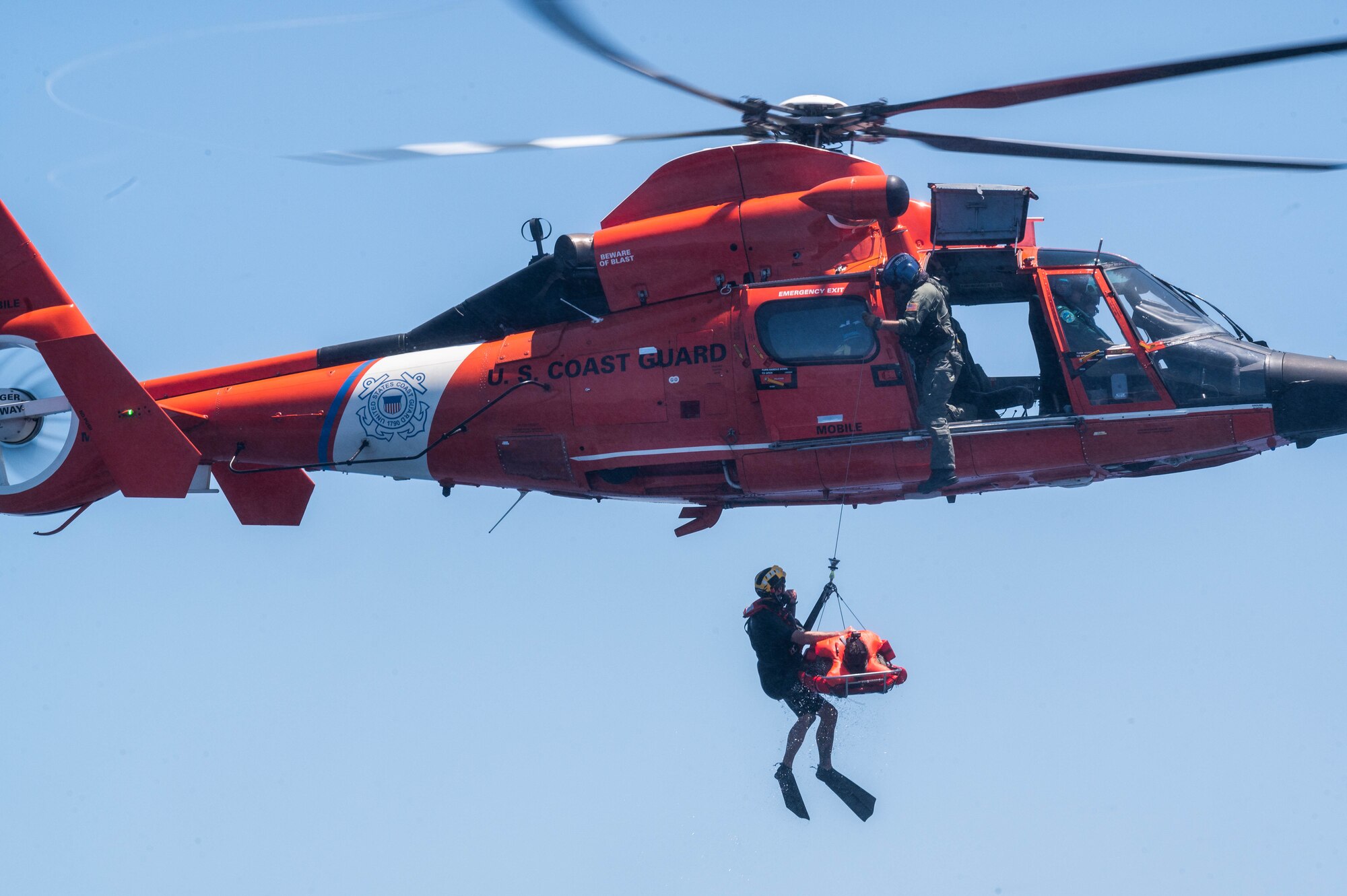 Pilot getting airlifted into a helicopter by a coast guard team.