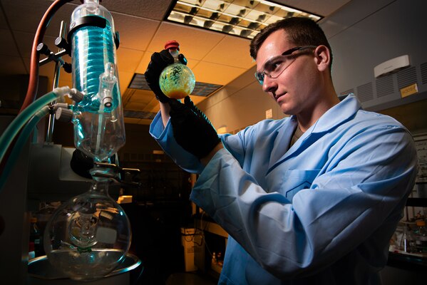 A man in a lab coat holds a flask.
