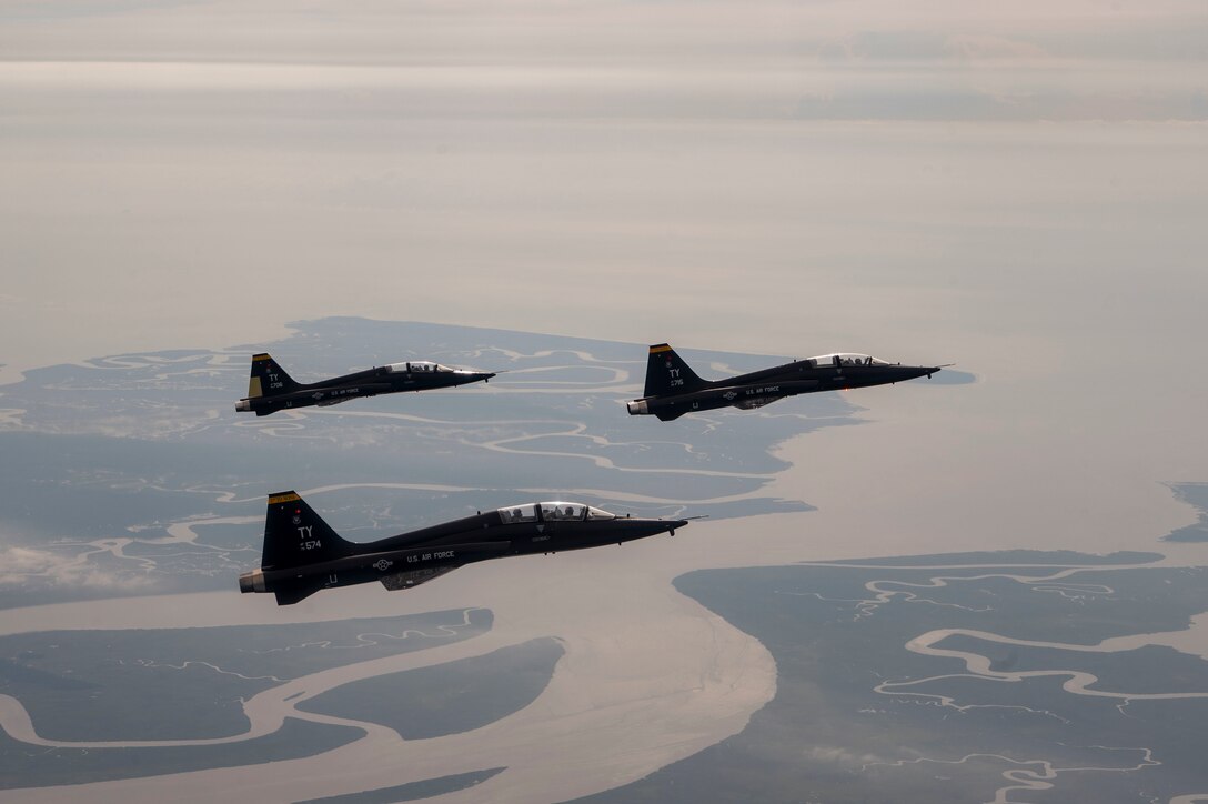 Three T-38A Talons fly over land and water.