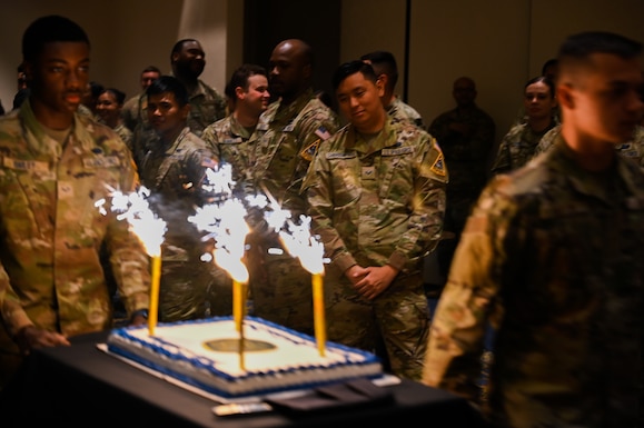 A cake with candles is wheeled into a room by people