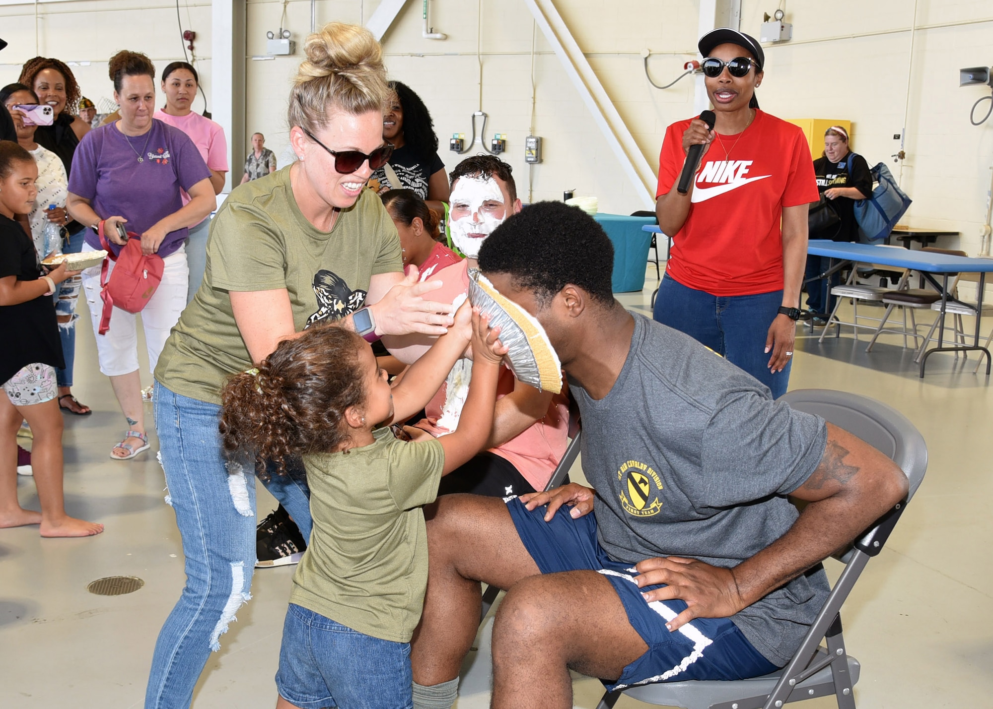 A child and woman smash a pie into Chief Anderson's face. Others look on in the background.