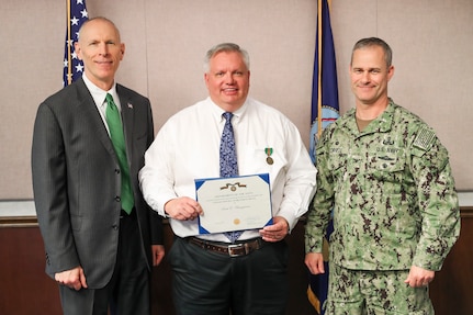 Scott Bumgarner (center) holds Navy Civilian Service Achievement Medal presented by NSWC IHD Commanding Officer Capt. Eric Correll (right) and NSWC IHD Technical Director Ashley Johnson