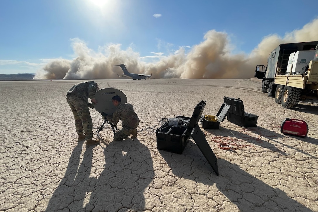 Two service members set up a satellite on parched ground.