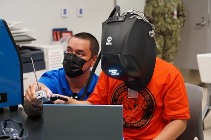 Clifford Ching (left), a welding skills instructor from Pearl Harbor Naval Shipyard and Intermediate Maintenance Facility (PHNSY & IMF) assists a James Campbell High School student using an arc welding simulator during a career-oriented field trip held in mid-April. This event is one of several PHNSY & IMF community outreach programs conducted with local schools. The visit gathered 26 students and three teachers from the school’s Science, Technology, Engineering, Arts, and Mathematics (STEAM) program that offers students insight in trade industry occupations. During the field trip, representatives from the shipyard’s Production Resource Training Department facilitated the students’ experience with a tour of its welding school including welding demonstrations and an overview of equipment and training facilities used in honing welding trade skills. (Official U.S. Navy photo by Justice M. Vannatta)