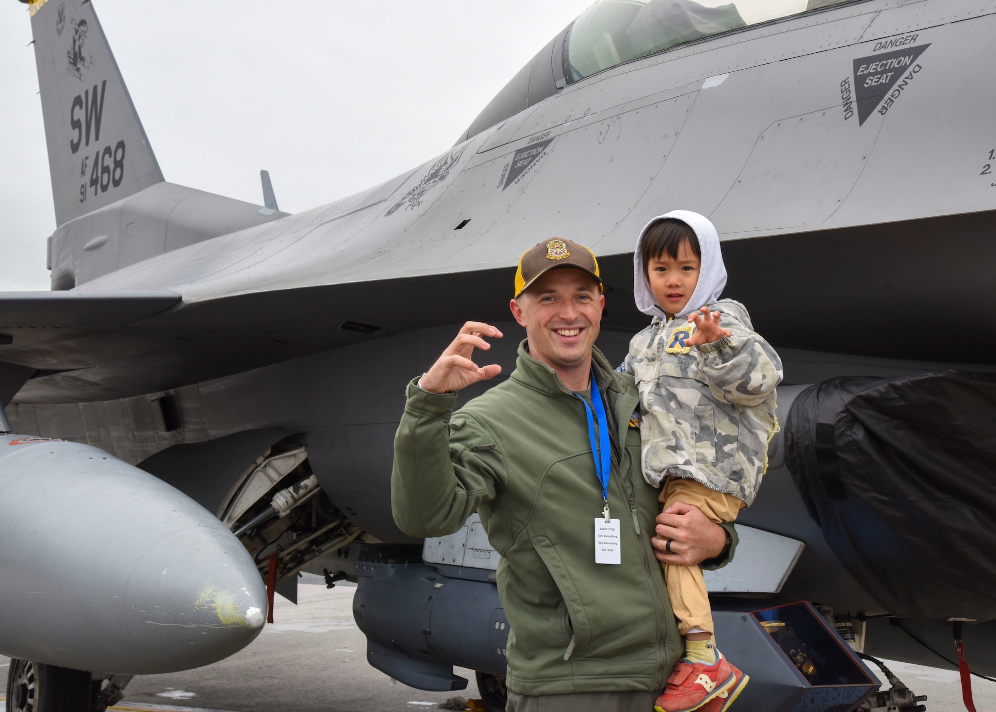 Skyfest 2022 attendees pose for a photo in front of a tiger stripe fighter jet static display at Fairchild Air Force Base, Washington, May 14, 2022. Team Fairchild held the Fairchild Skyfest 2022 airshow as a means of thanking the local community for their support and partnerships, as well as to inspire future generations of Airmen with a showcase of U.S. Air Force assets and their capabilities. (U.S. Air Force photo by Senior Airman Anneliese Kaiser)