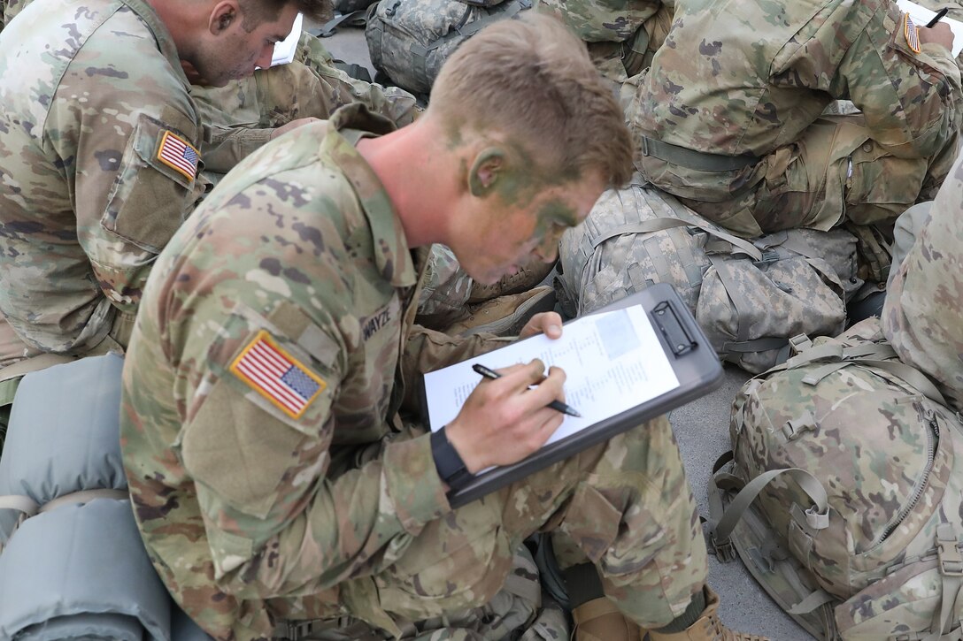 A soldier writes on a paper attached to a clipboard.