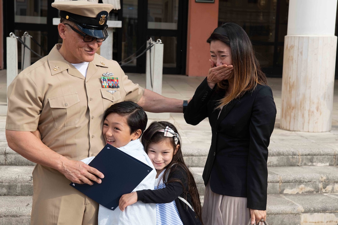 Two children hug a sailor.