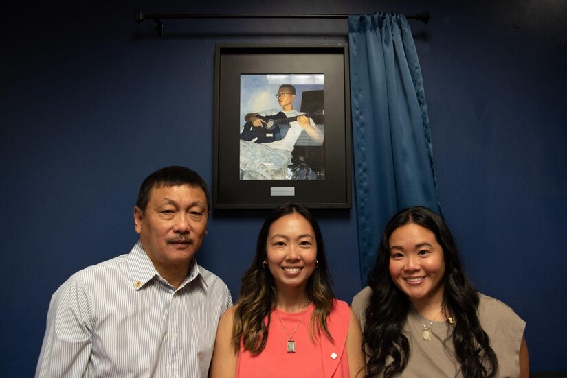 A man and two women pose in front of a photo of U.S. Staff Sgt. Franklin Kaunang