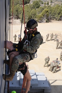 Soldier rappels on side of building with dummy attached simulating a casualty