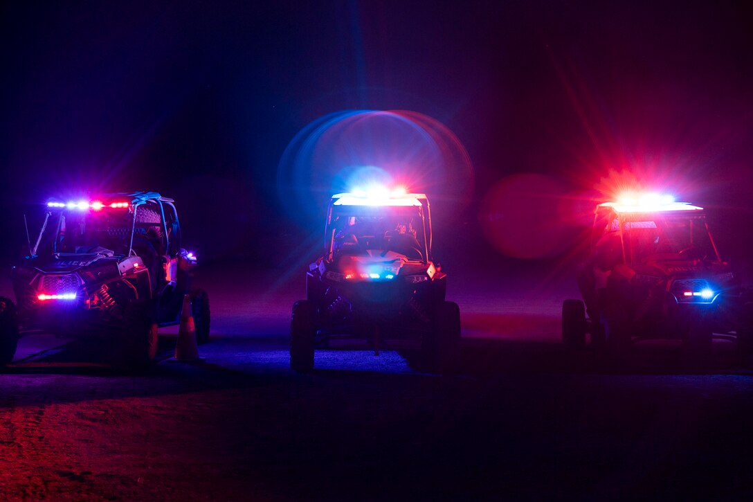 Three off-road vehicles park next to each other illuminated with red and blue lights.