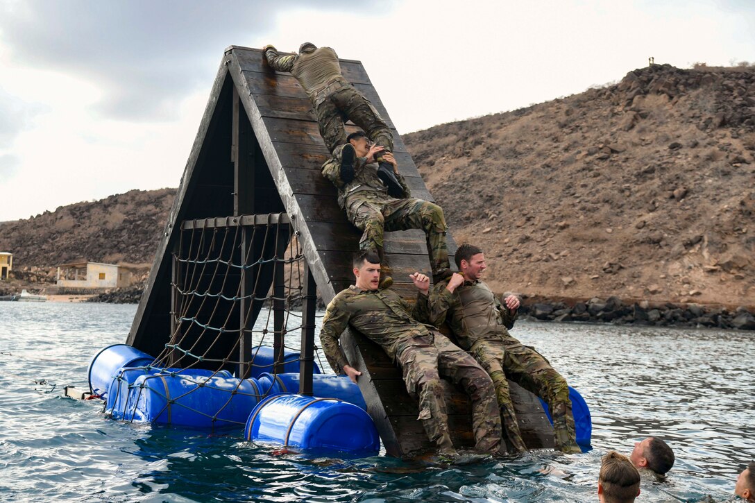 Service members form a pyramid to climb over an obstacle in a body of water.