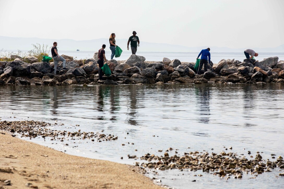 Sailors carrying green trash bags walk on a long piles of rocks.