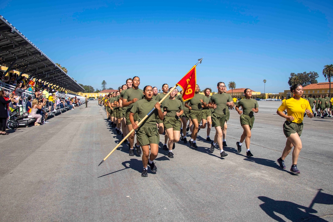A group of Marines run in formation in front of a crowd.