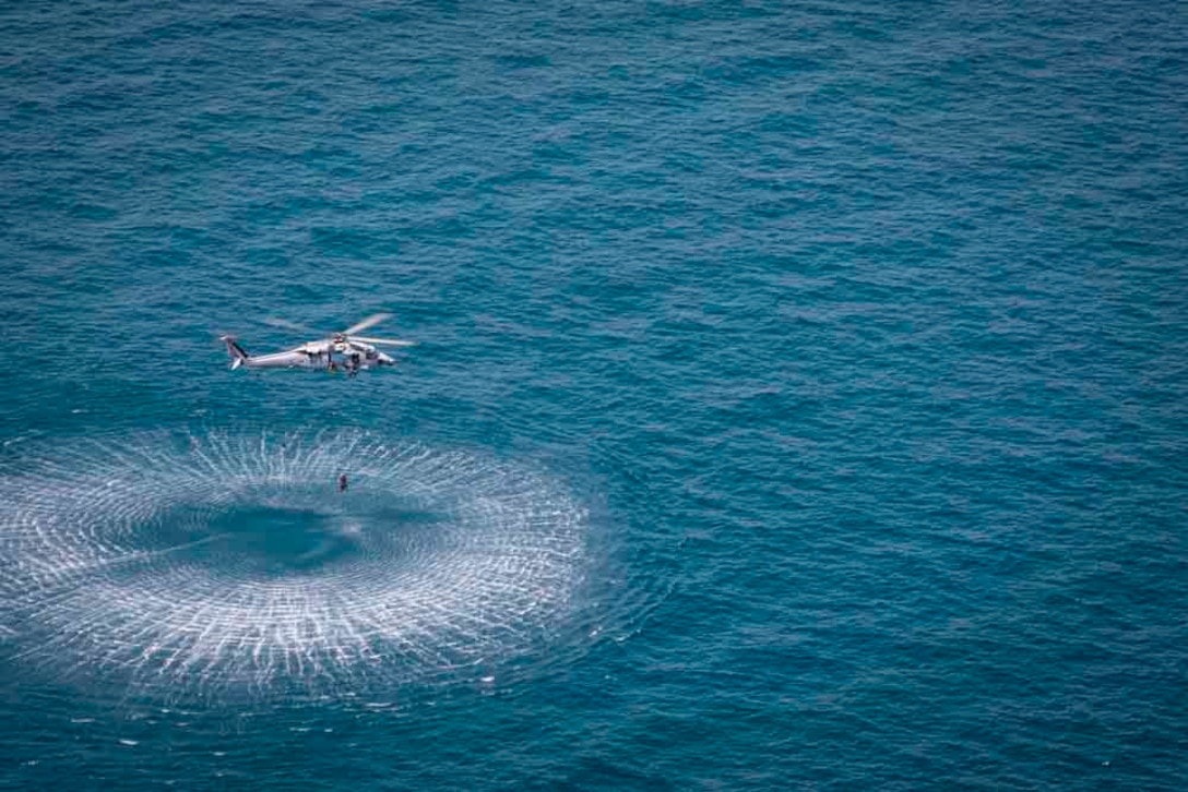 A sailor hangs from a rope from an airborne helicopter.