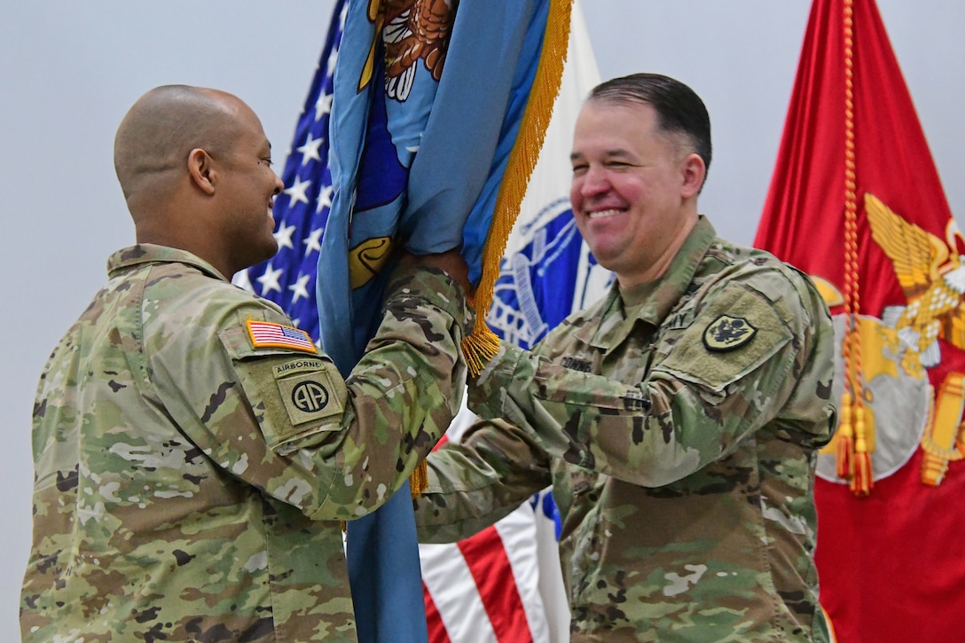 A man in a uniform passes a unit flag off to another man in uniform as part of a change of command ceremony