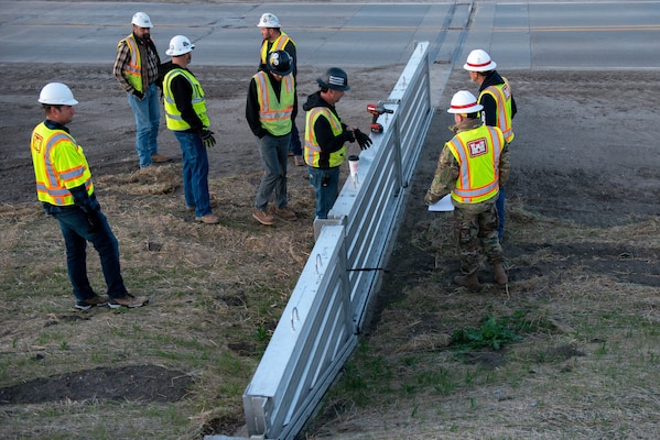 Traffic is directed through during the installation of flood gate panels along the highway leading to Hamburg Iowa, 24 Apr., 2022.