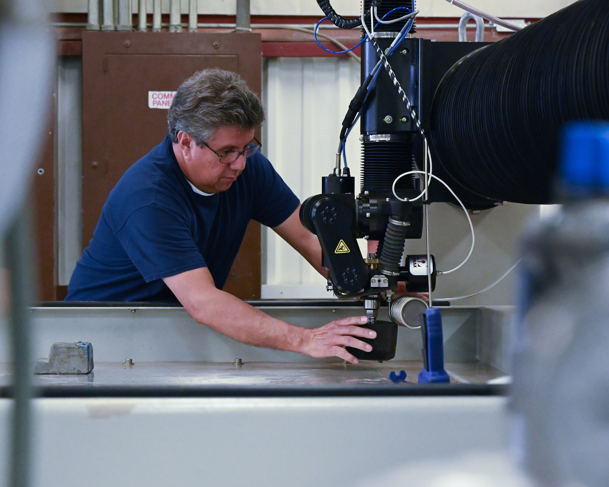 Arnold Becerra, 47th Flying Training Wing machinist, adjusts the safety guard of the water jet head at Laughlin Air Force Base, Texas, on April 26, 2022. The water jet has a linear accuracy range of .001 mm to .025 mm. (U.S. Air Force photo by Airman 1st Class Keira Rossman)