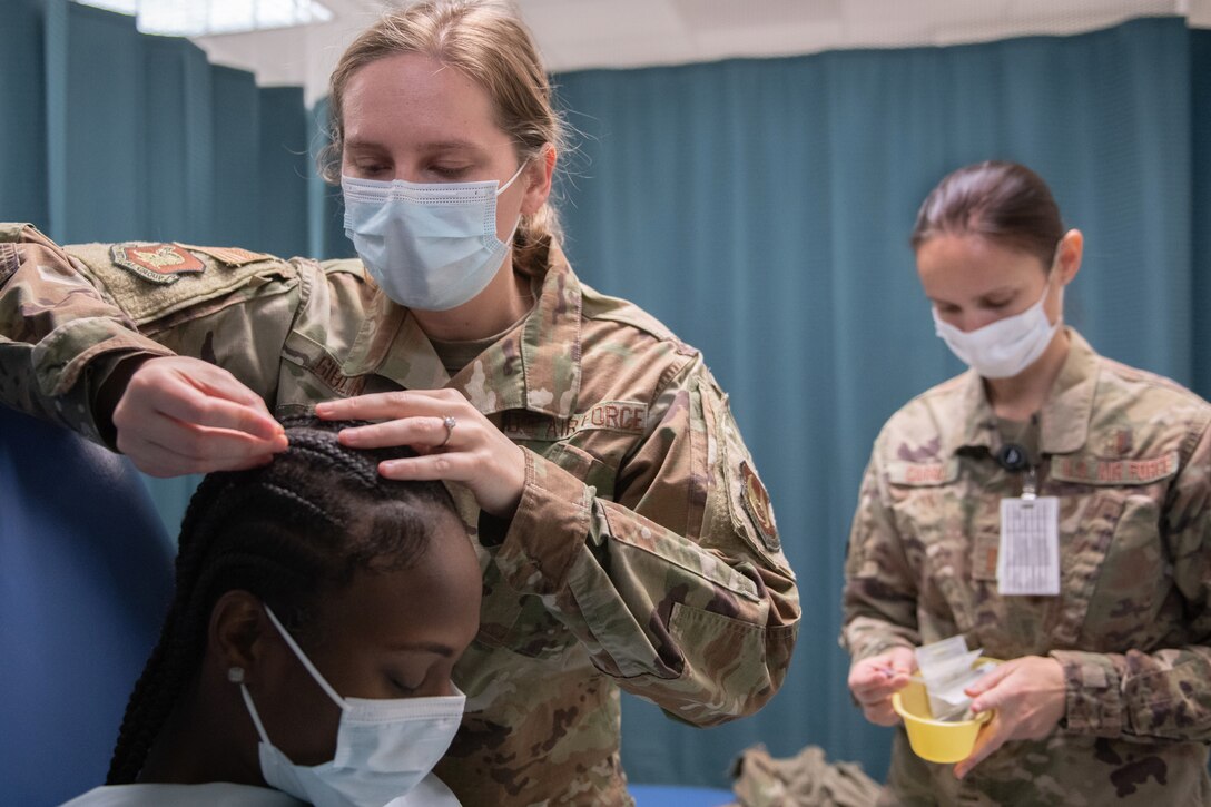 An airman puts a needle into a person's scalp.