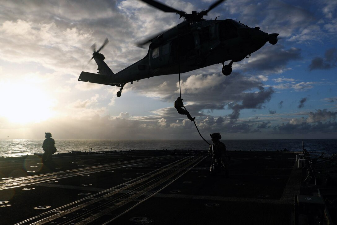 Sailors rappel from a helicopter onto the deck of a ship.