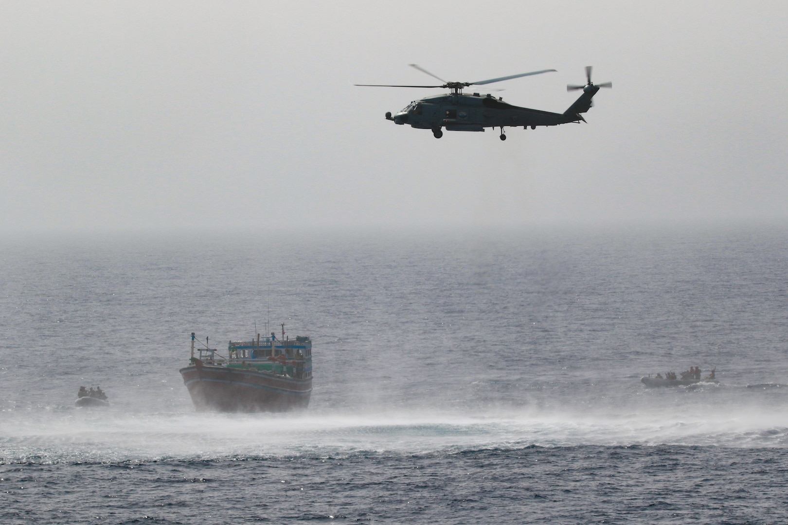 220516-N-TT059-1005 GULF OF OMAN (May 16, 2022) An MH-60R Seahawk from Helicopter Maritime Strike Squadron (HSM) 35, Detachment 1, provides aerial support to an interdiction team from guided-missile destroyer USS Momsen (DDG 92) approaching a fishing vessel May 16. The vessel was seized while transiting international waters in the Gulf of Oman.