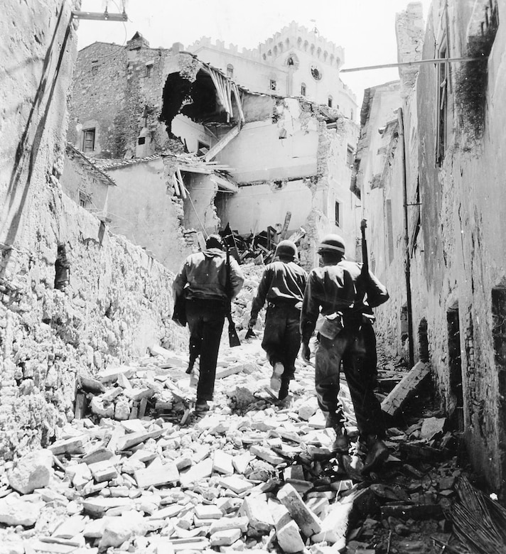Three men walk up a rubble-covered street.