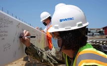 Woman Navy officer in hard hat signs a steel construction beam.