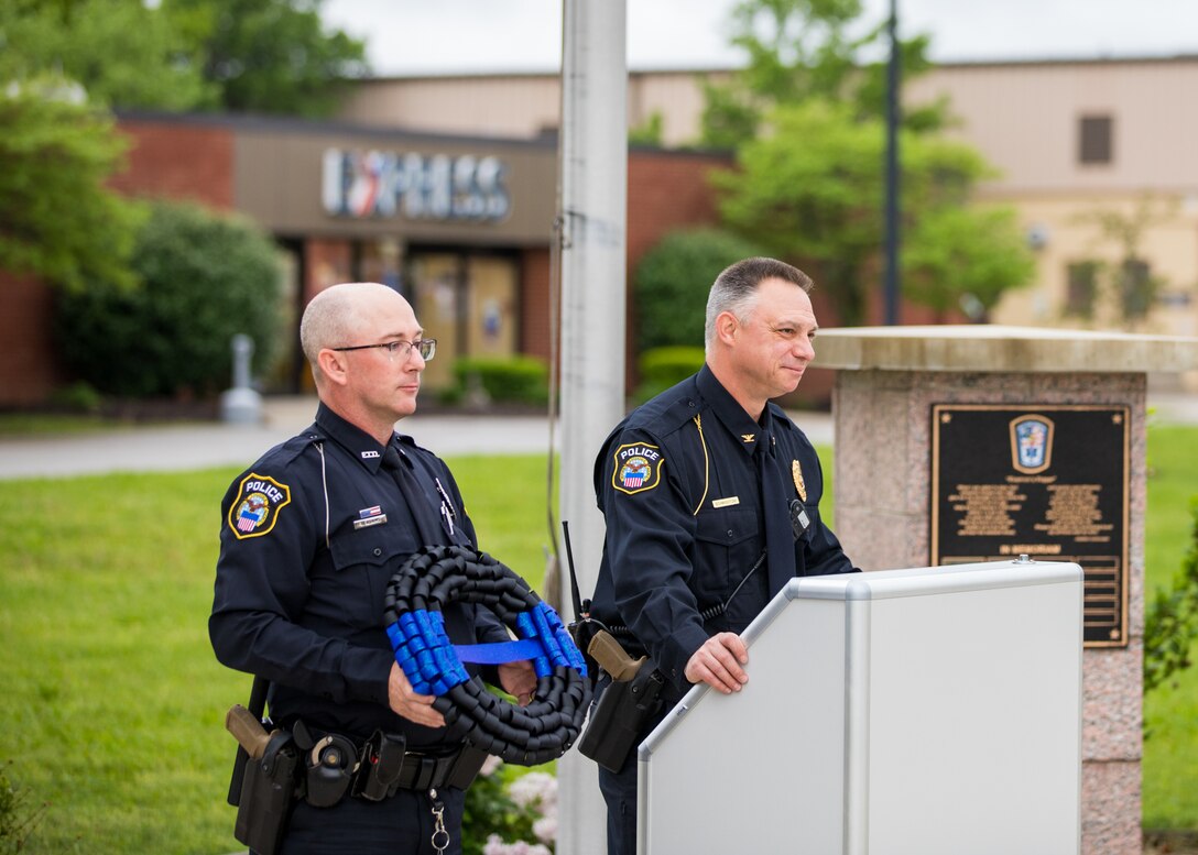 Two police officers. One at a outdoor podium and the other holding a wreath.