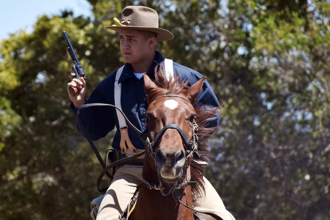 A soldier dressed in a cavalry uniform holds a gun while riding a horse.