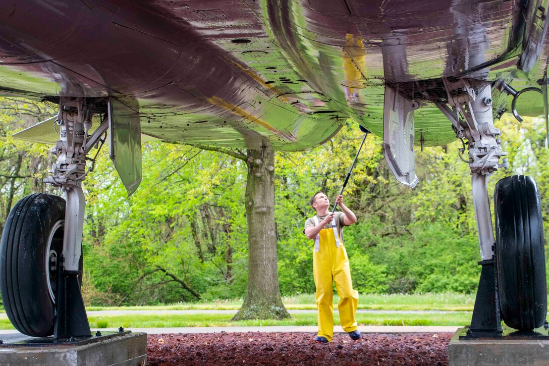 An airman cleans underneath a large aircraft.