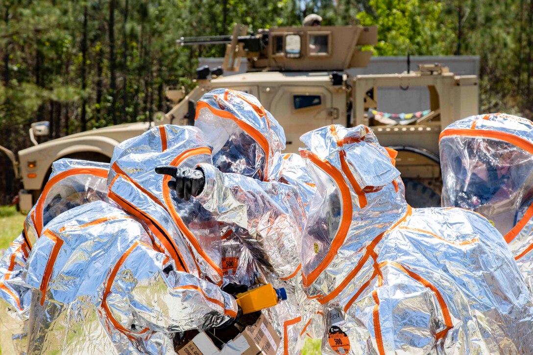 Soldiers wearing protective gear stand in a huddle.