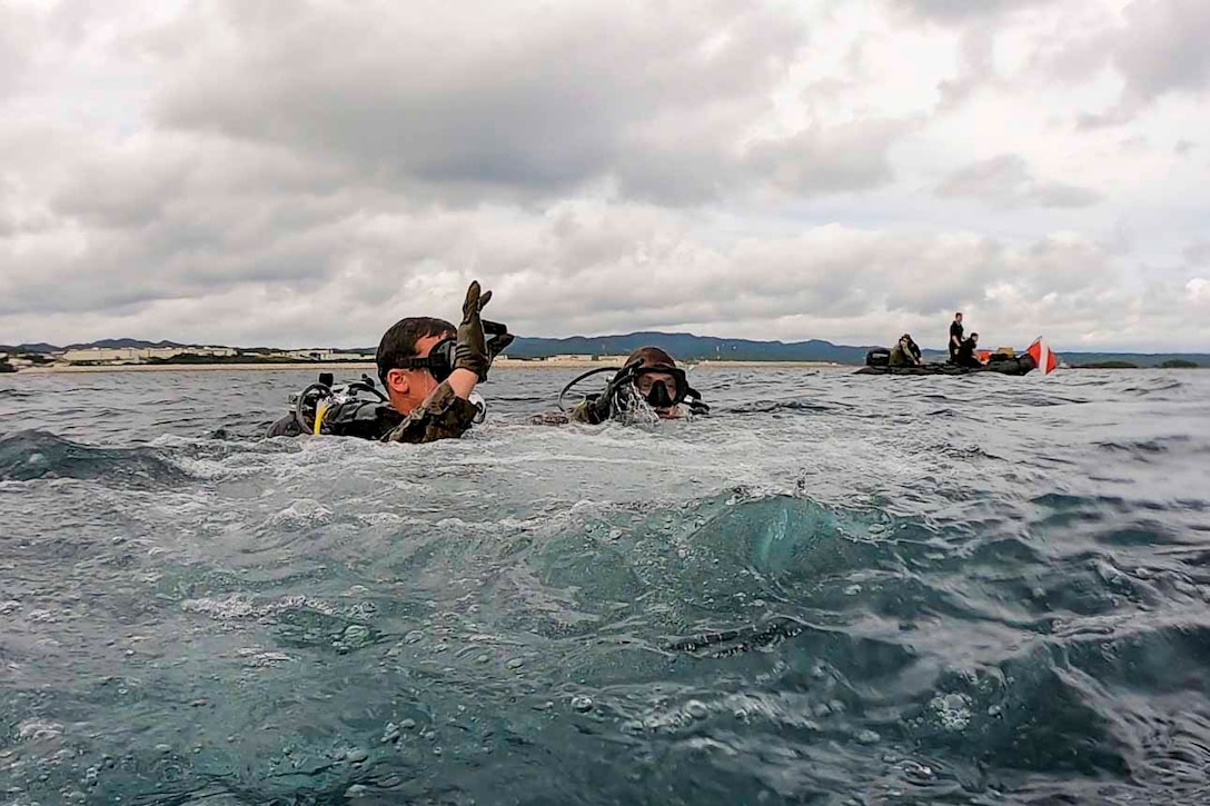 Marines wearing dive gear move through waters.