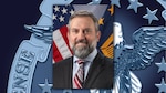 Close up of a man in a suit sitting in front of flags